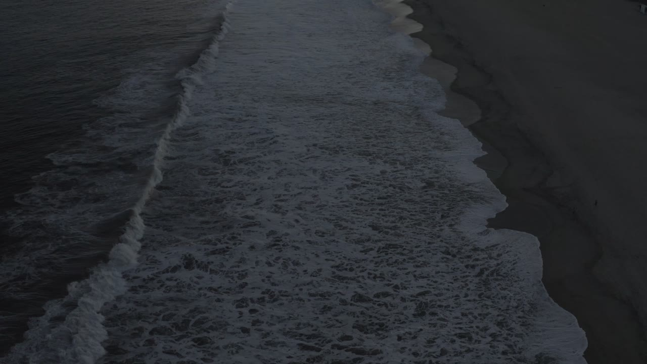 A broad band of white foam pushes closer to the sand in Los Cabos, with dark water filling the left side and no visible people.