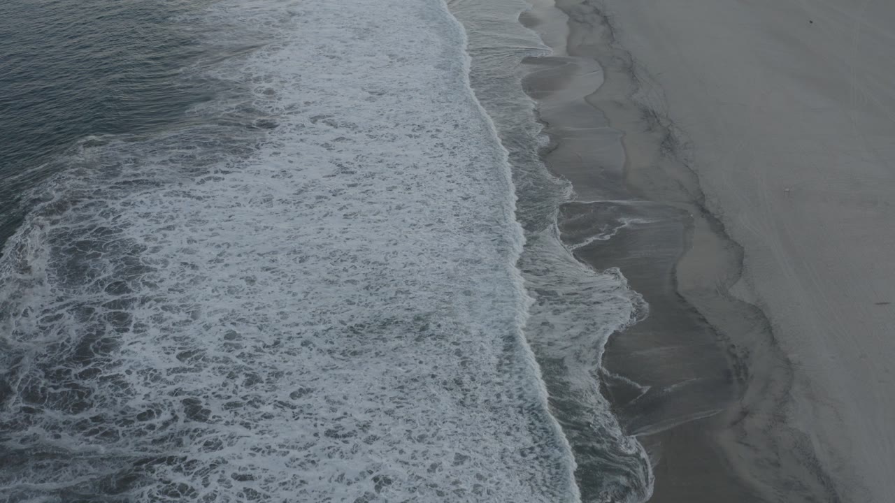 Overhead surf breaking along a gray sandy beach.
