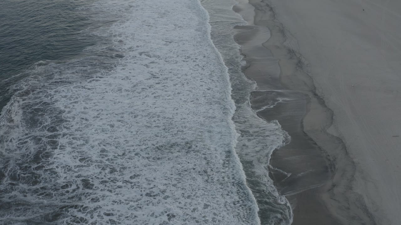 Aerial Los Cabos shoreline frame with the white wave band slightly farther up the beach and dark wet-sand channels visible beside the foam.