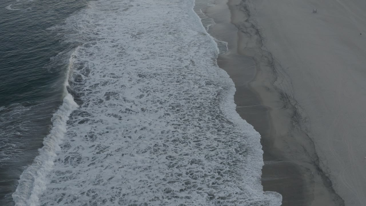Overhead shoreline with waves breaking beside open sand.