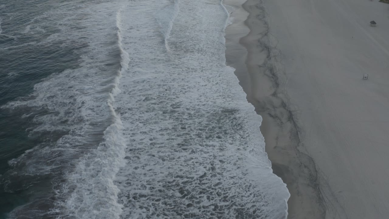 Aerial shoreline with foam bands and open beach.