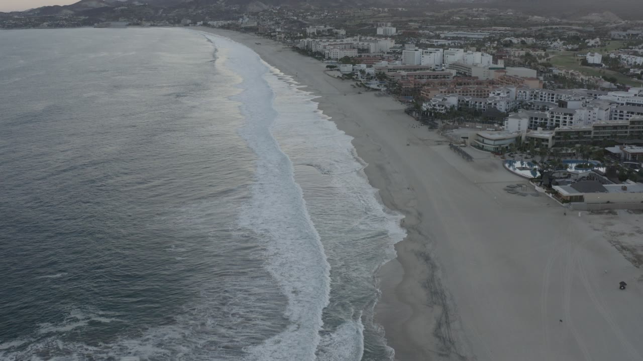 Aerial view of waves along a wide beach beside coastal buildings.