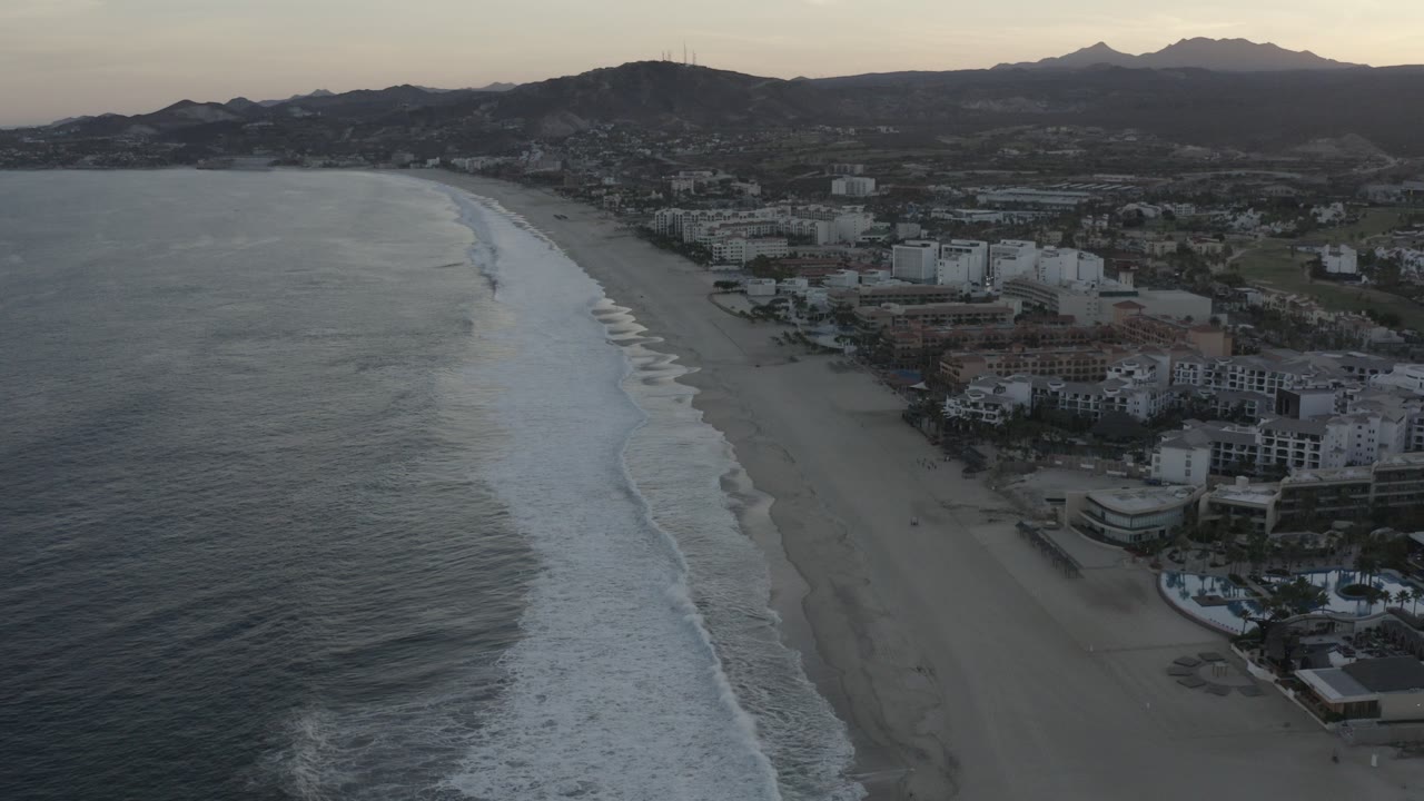 Aerial view of surf, beach, beachfront buildings, and mountains.