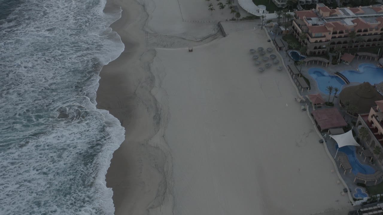 Aerial view of surf beside a sandy beach and beachfront condominiums.