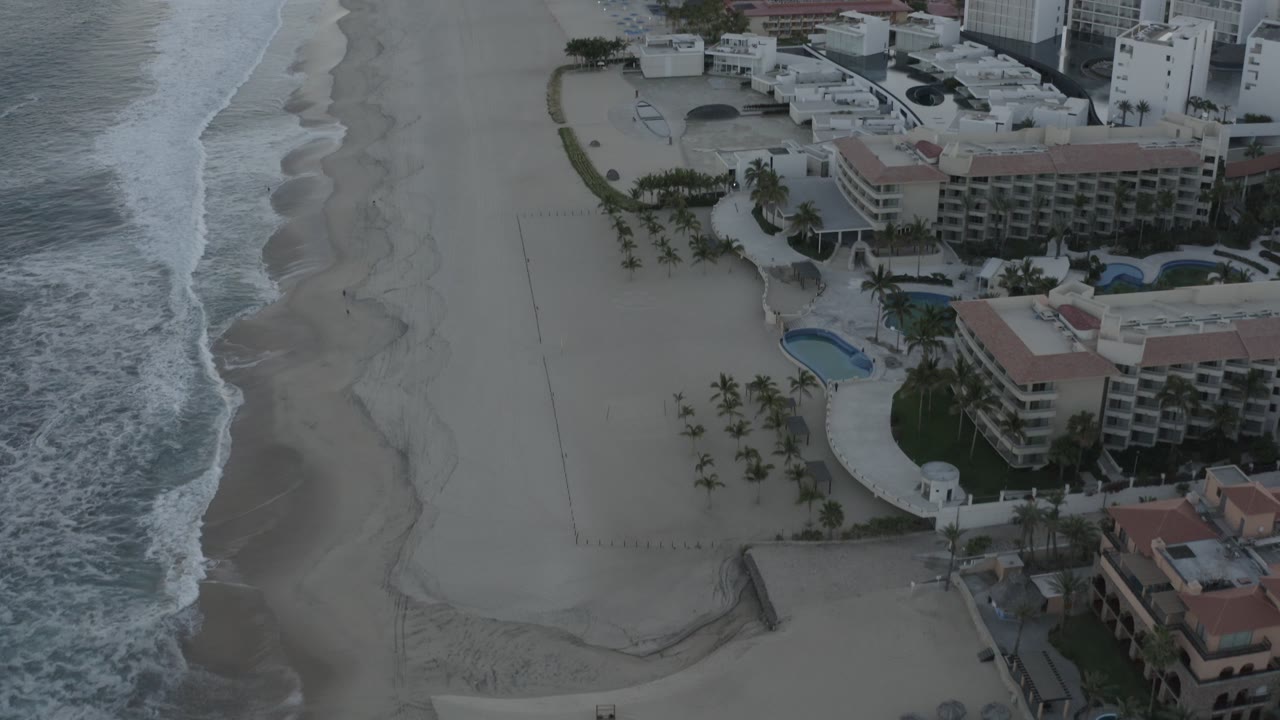 Beachfront hotels and pools seen from above beside foamy surf.