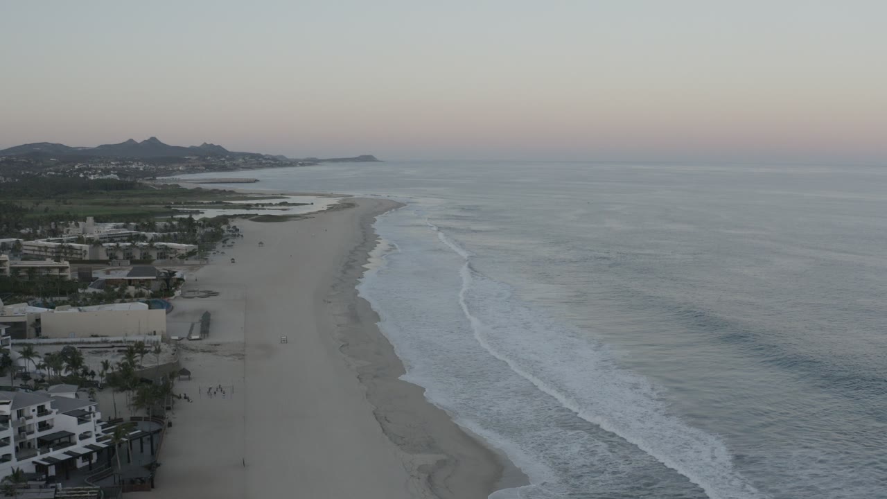 Elevated view of waves rolling beside a long beach at sunrise.