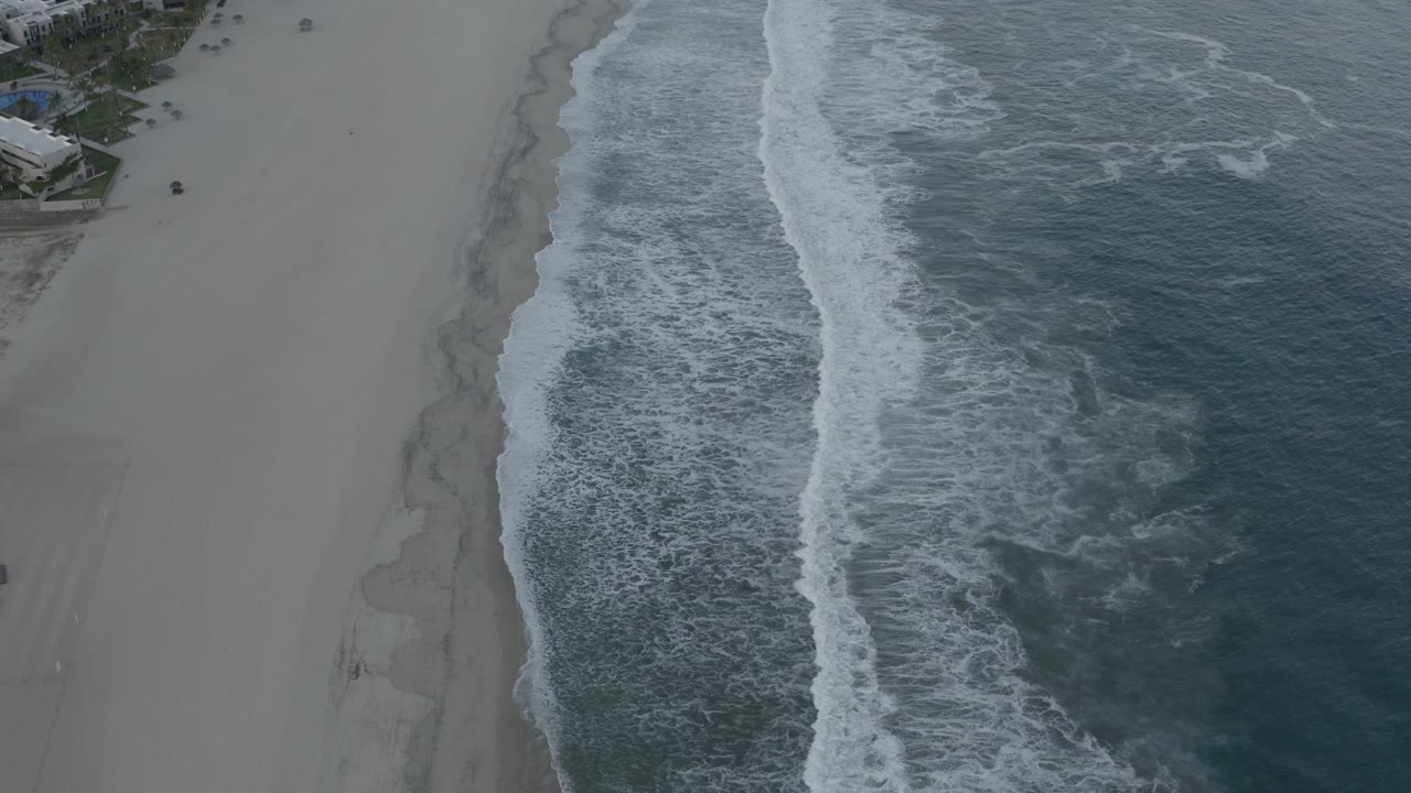 Aerial view of waves breaking beside a wide sandy beach.