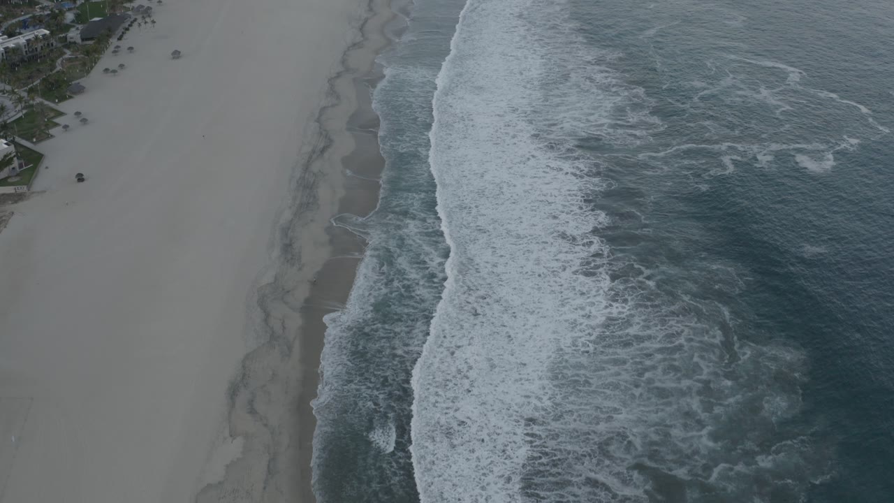 Drone-like side view of waves washing onto an empty beach.