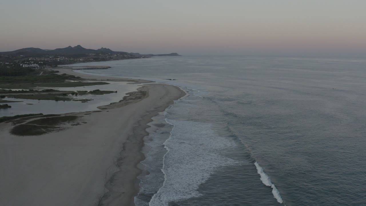 Aerial view of a long beach with waves and inland water at low light