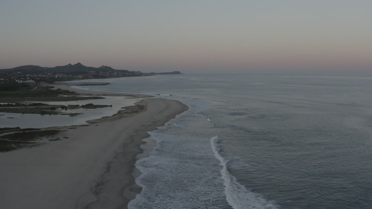 High aerial view of the Los Cabos shoreline, showing a long pale sandbar between calm inland water and darker ocean surf, with no visible people.