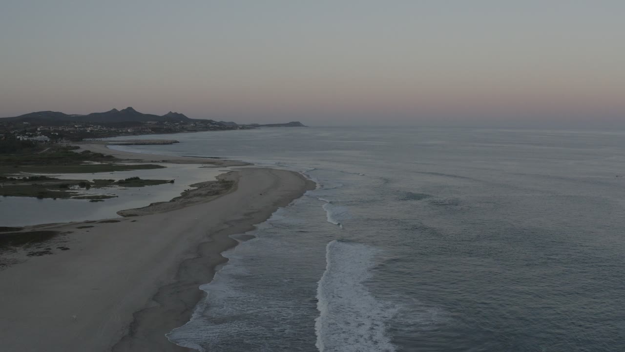 Aerial view of a curving sandy beach and gray-blue ocean.