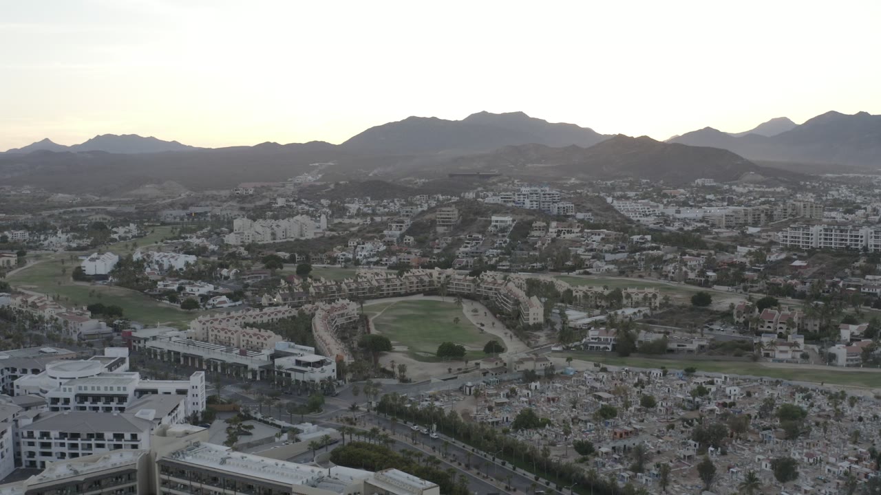 Aerial view of buildings, cemetery grounds, green fields, and mountains.