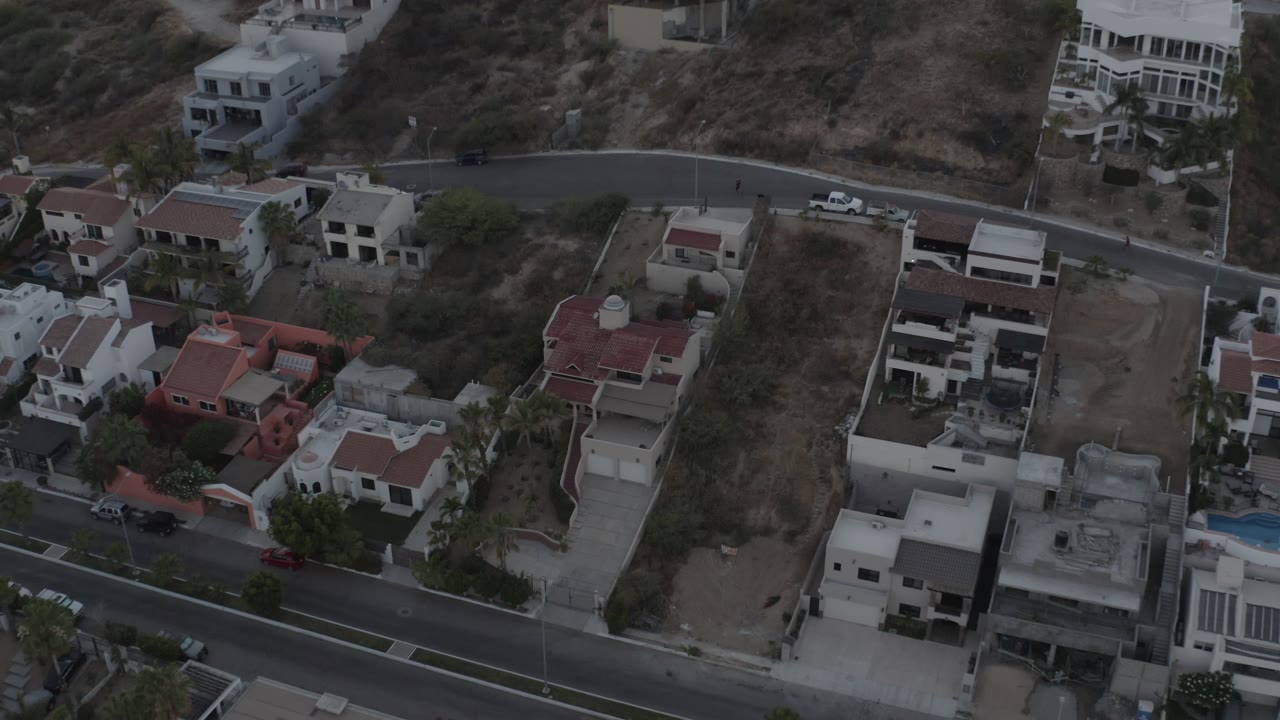 Drone view of modern homes beside a dry hillside road.