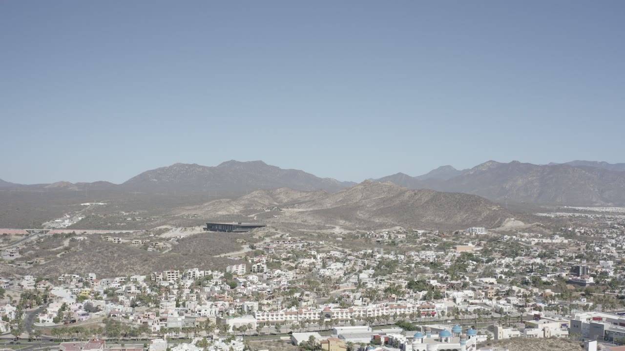 Wide hillside townscape with white buildings, arid slopes, and clear sky.