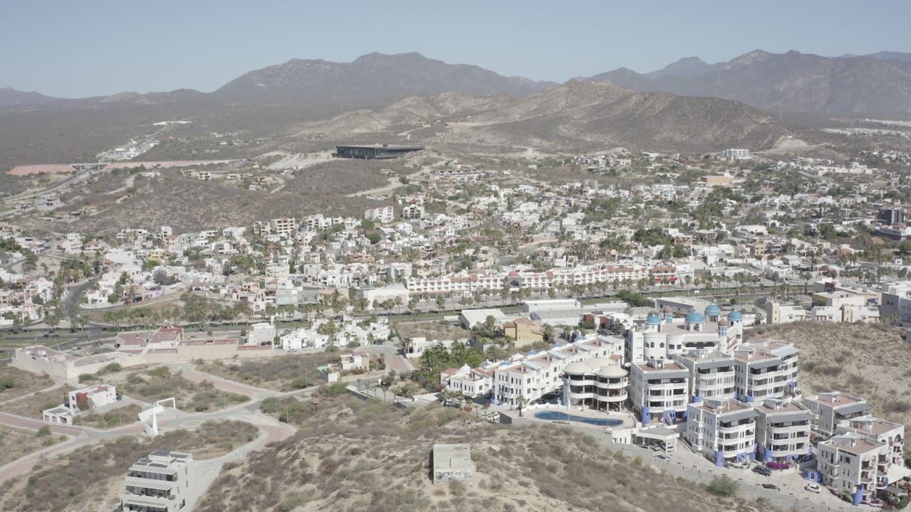 Aerial view of hillside homes, roads, scrub, and mountains under a clear sky.