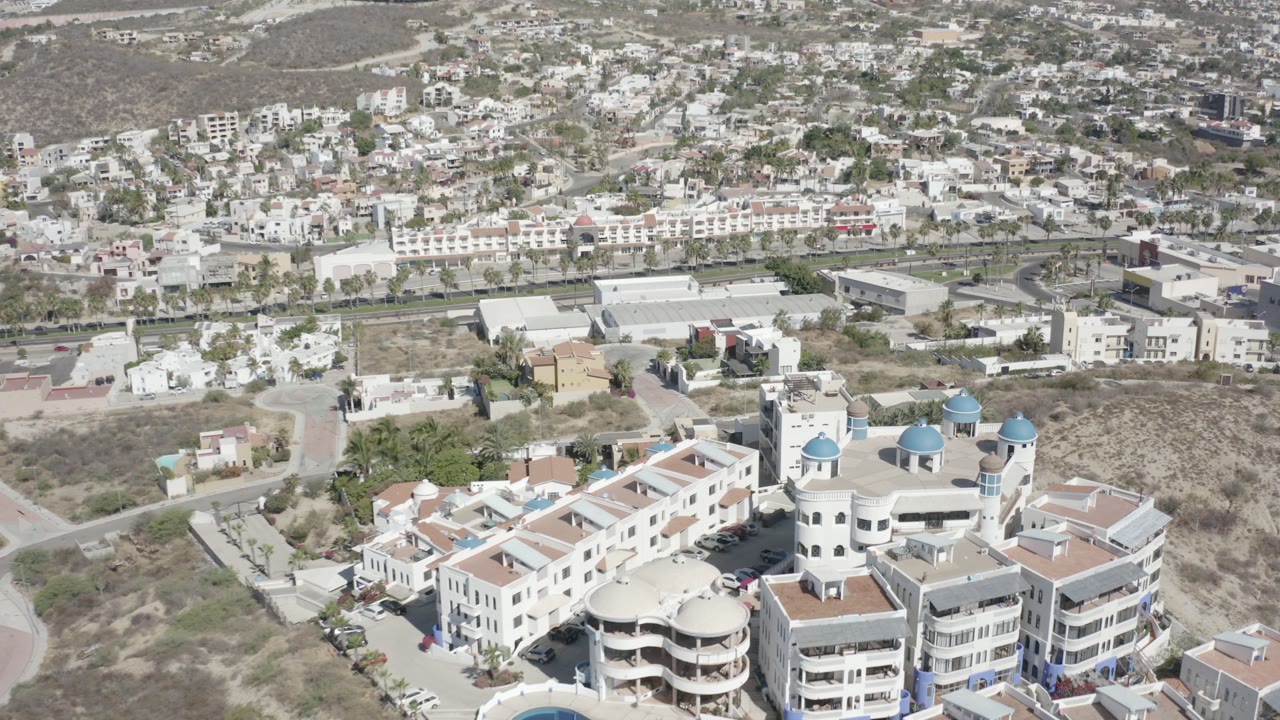 Aerial view of white buildings with blue domes near roads and hillside homes.