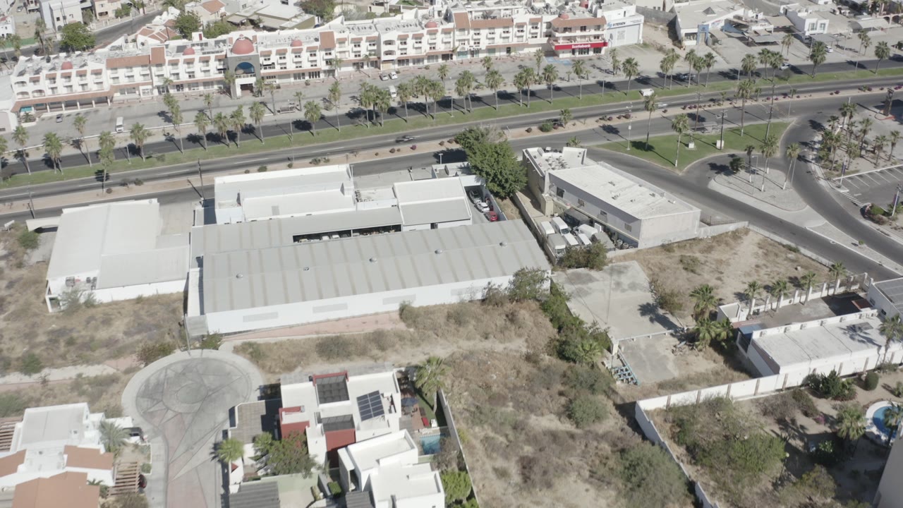 Aerial view of white flat-roof buildings beside a divided road and palm median.