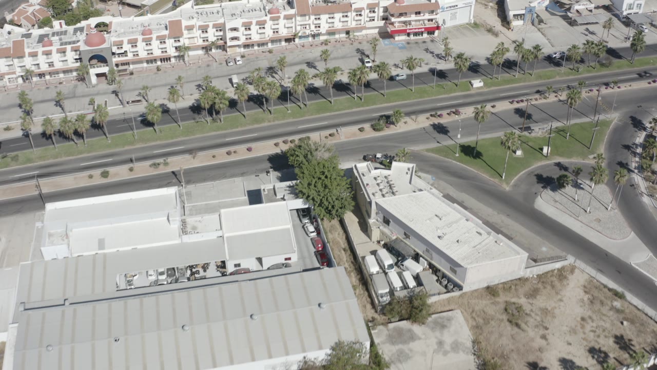 Aerial view of low-rise buildings, a divided road, palm trees, and cars.