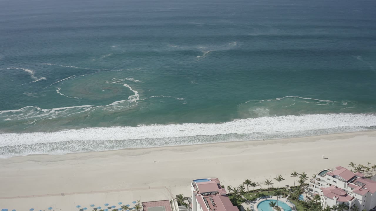 Aerial view of turquoise ocean waves breaking onto a pale sandy beach.