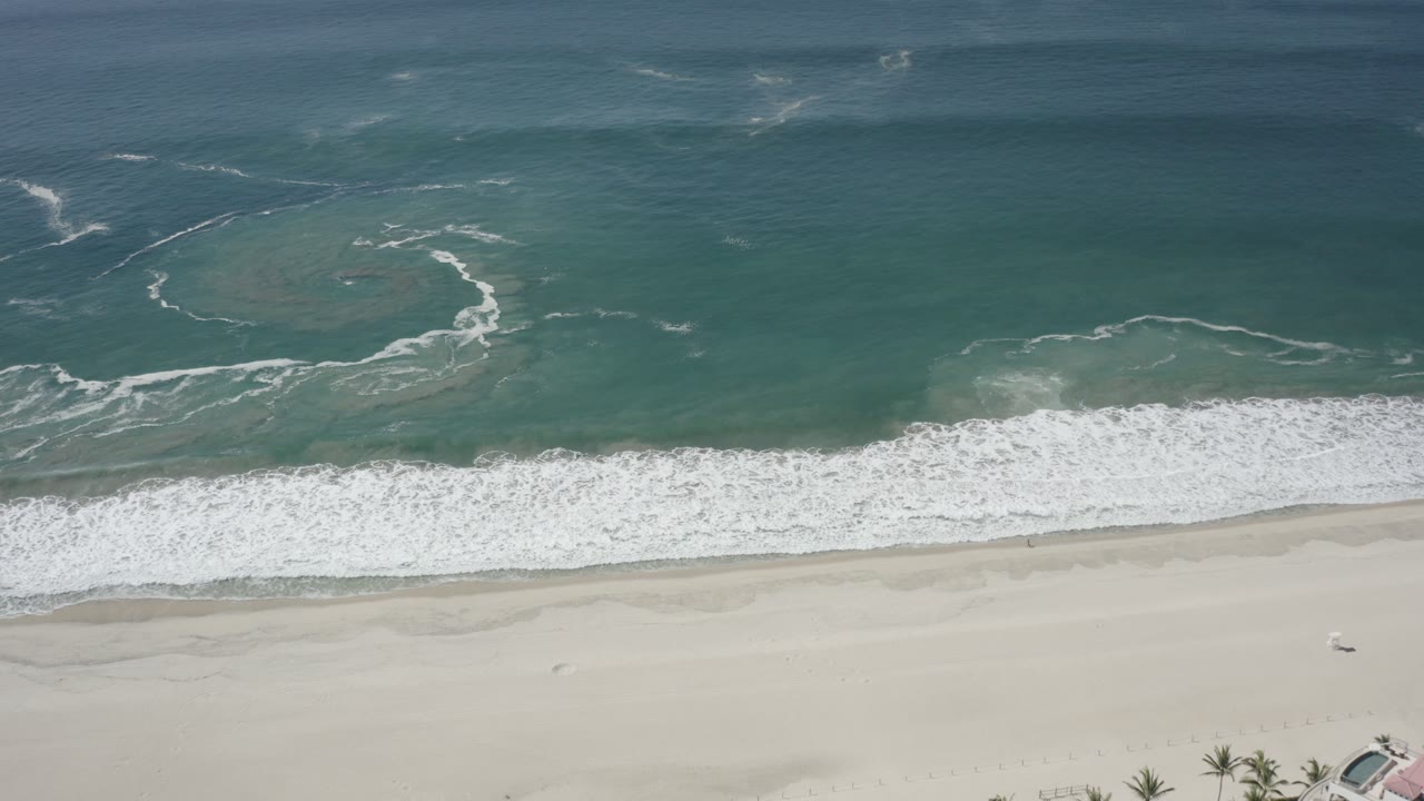 Aerial view of teal ocean waves breaking onto pale sand.