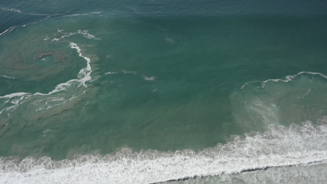 Top-down ocean water with a broad white wave band across the lower frame.