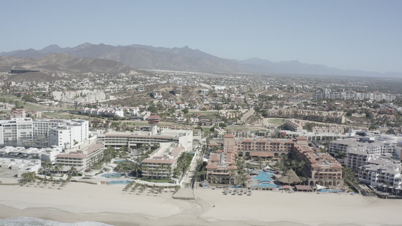 Wide coastal aerial with resorts, beach, town, and mountains