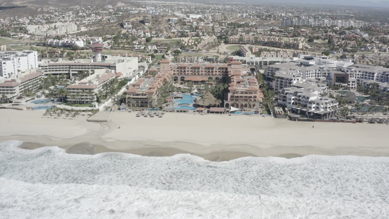 Aerial beachfront with surf, sand, and resort buildings.