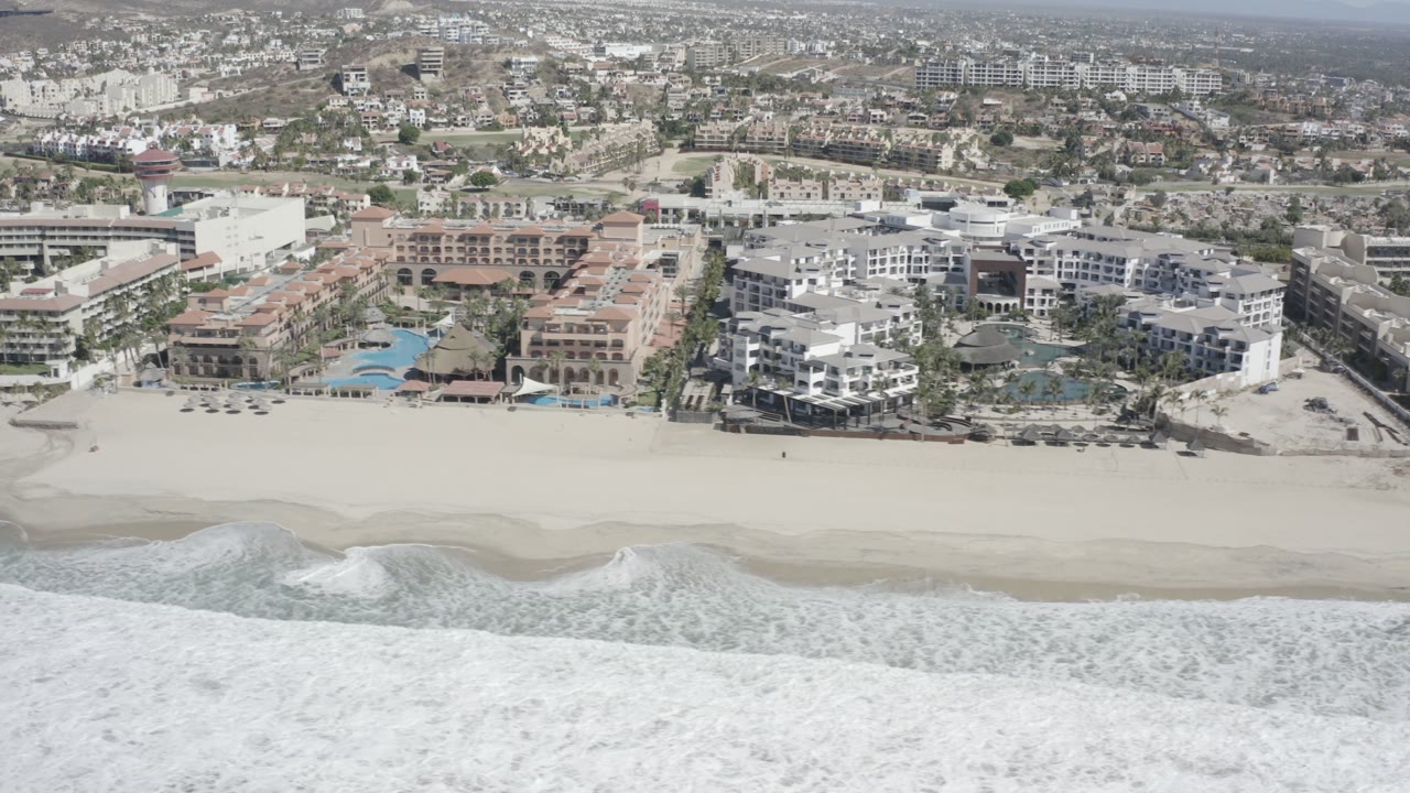 Wide aerial coastline with surf, sand, resorts, and inland town blocks.