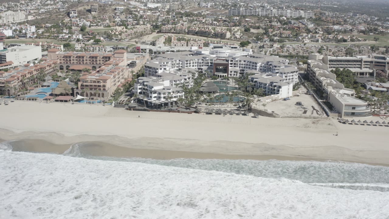 Aerial view of surf, sandy beach, beachfront resorts, and town buildings.