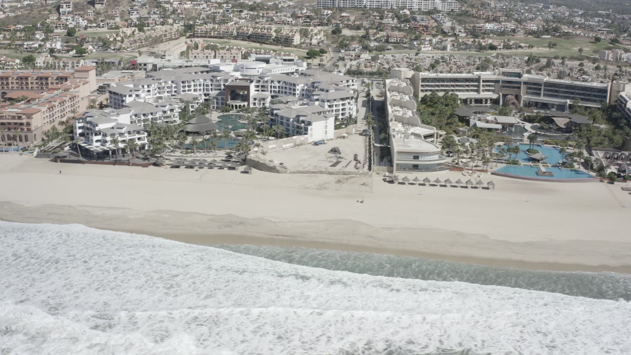 Drone-style view of beach resort complex beside breaking waves.