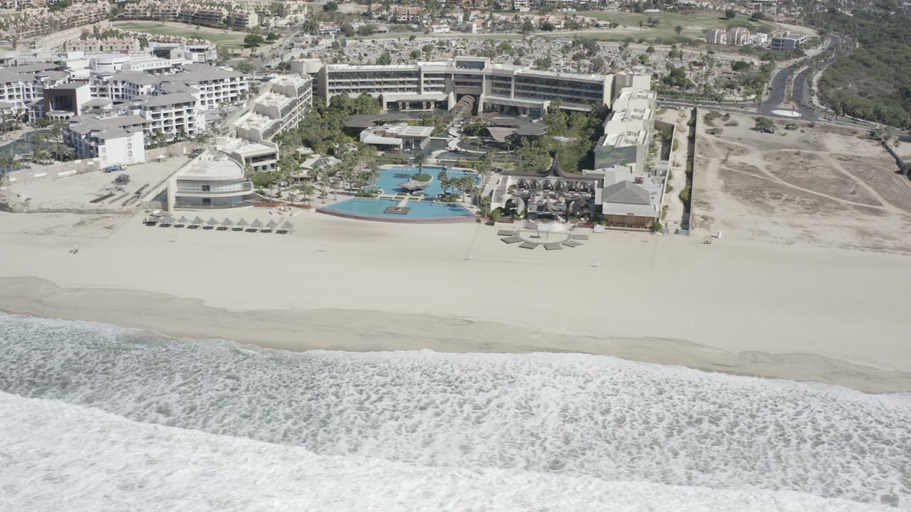 Drone view of beach frontage, pools, roads, and waves.