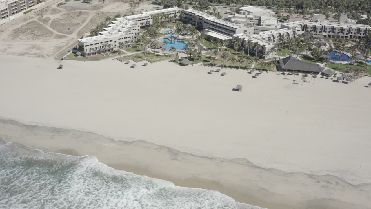 Aerial view of surf, wide sand beach, and beachfront buildings.
