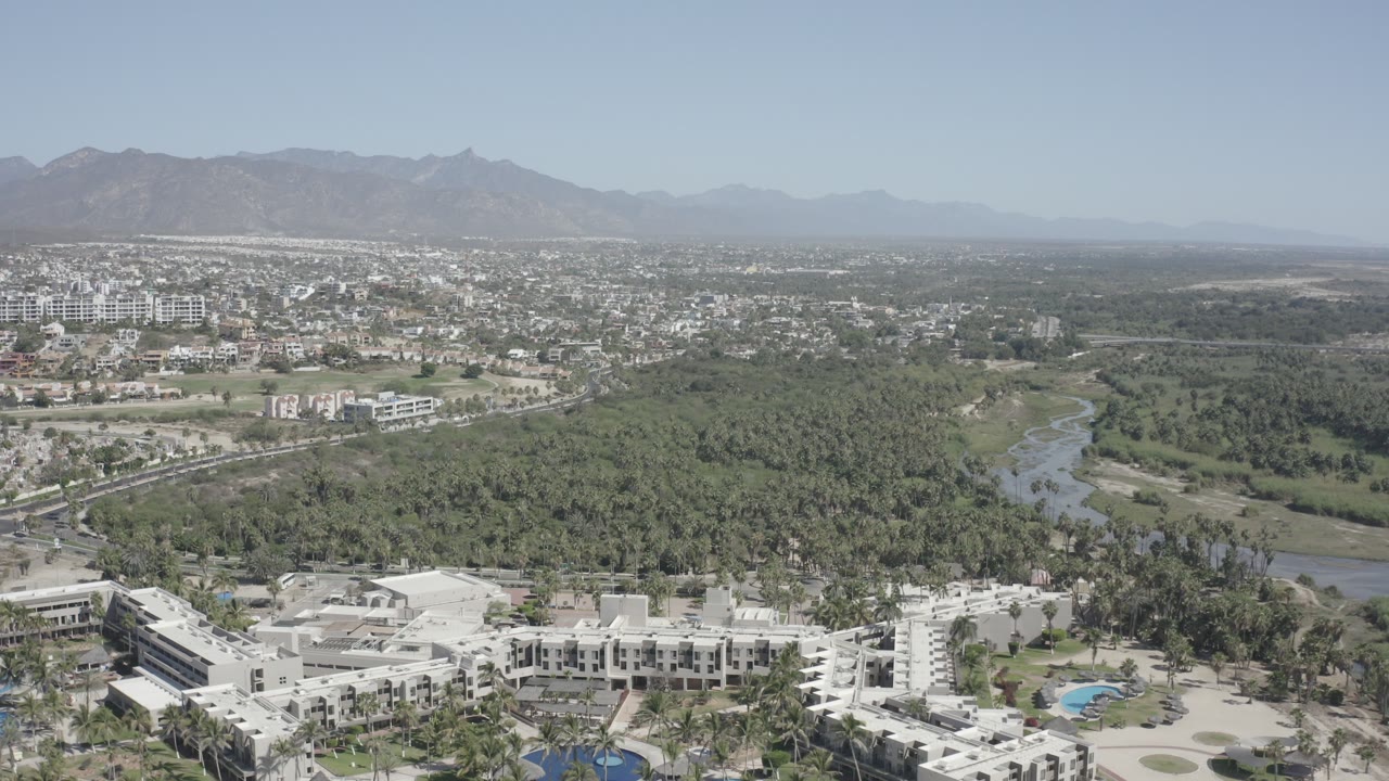 Aerial view of white buildings, dense trees, winding water, city blocks, and distant mountains.