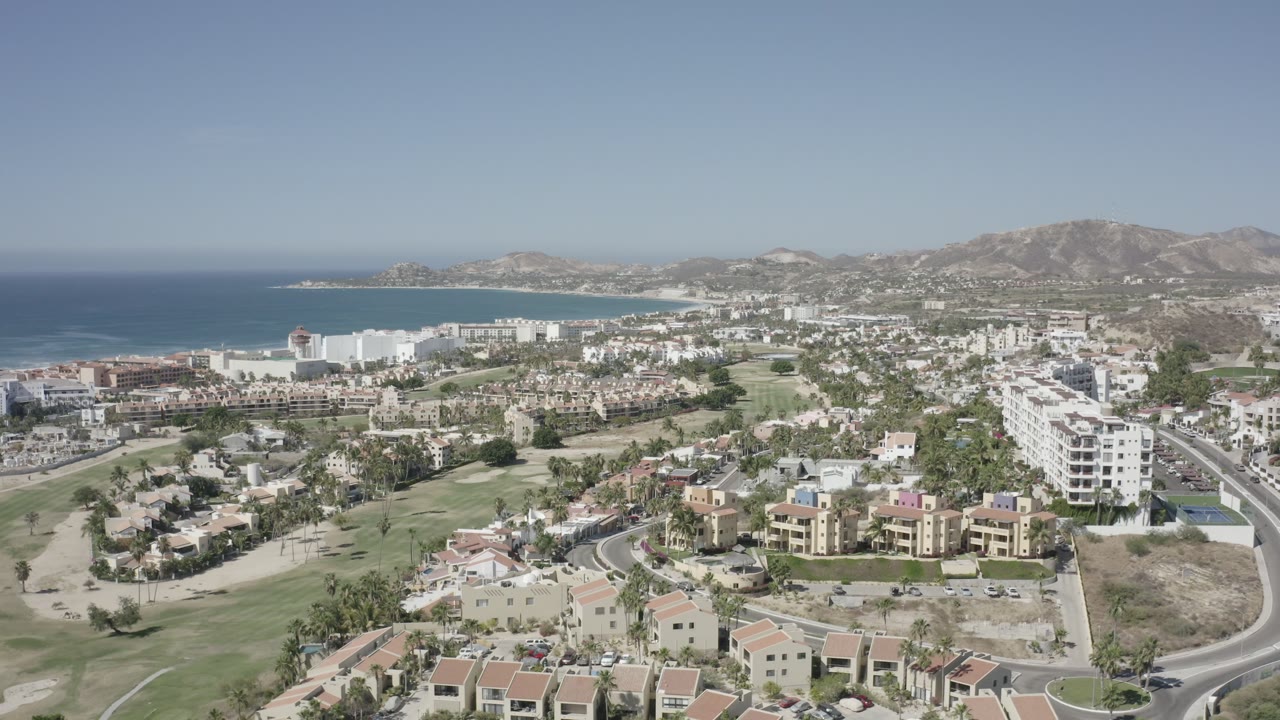 Aerial view of coastal town, ocean, green lawns, and hills.