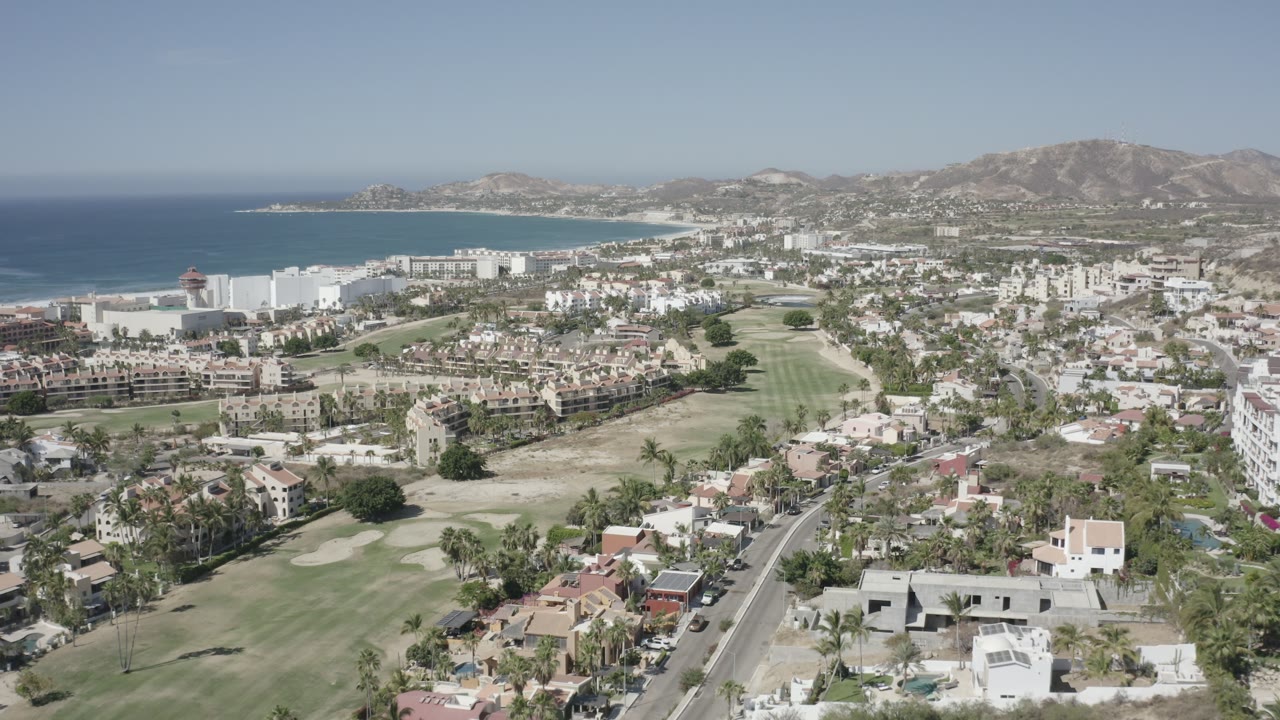 Drone-style view of a coastal neighborhood, golf course, bay, and arid hills.