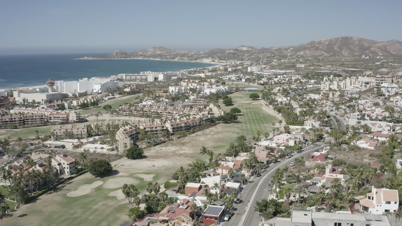 Aerial view of coastal city, golf course, shoreline, and mountains.