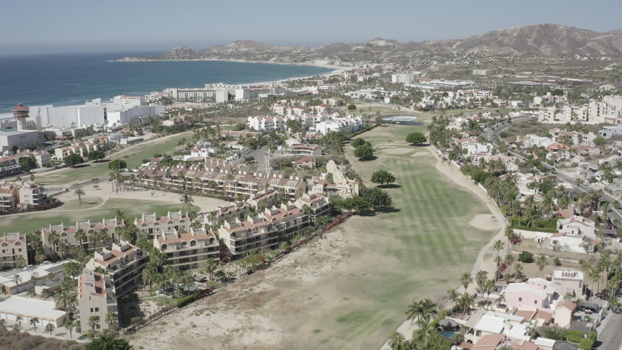 Drone-like view over coastal city blocks and a golf course.