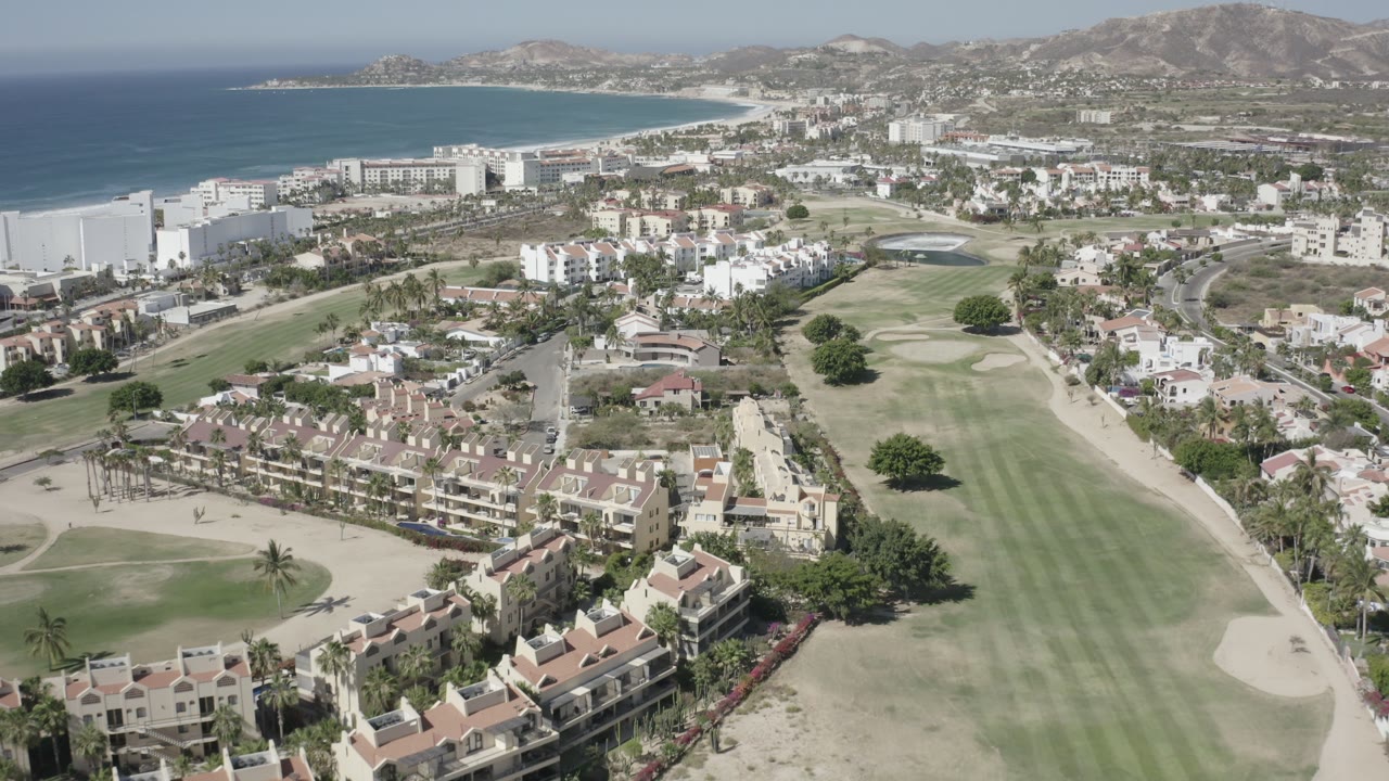 Aerial view of homes, golf fairways, beach, bay, and hills.