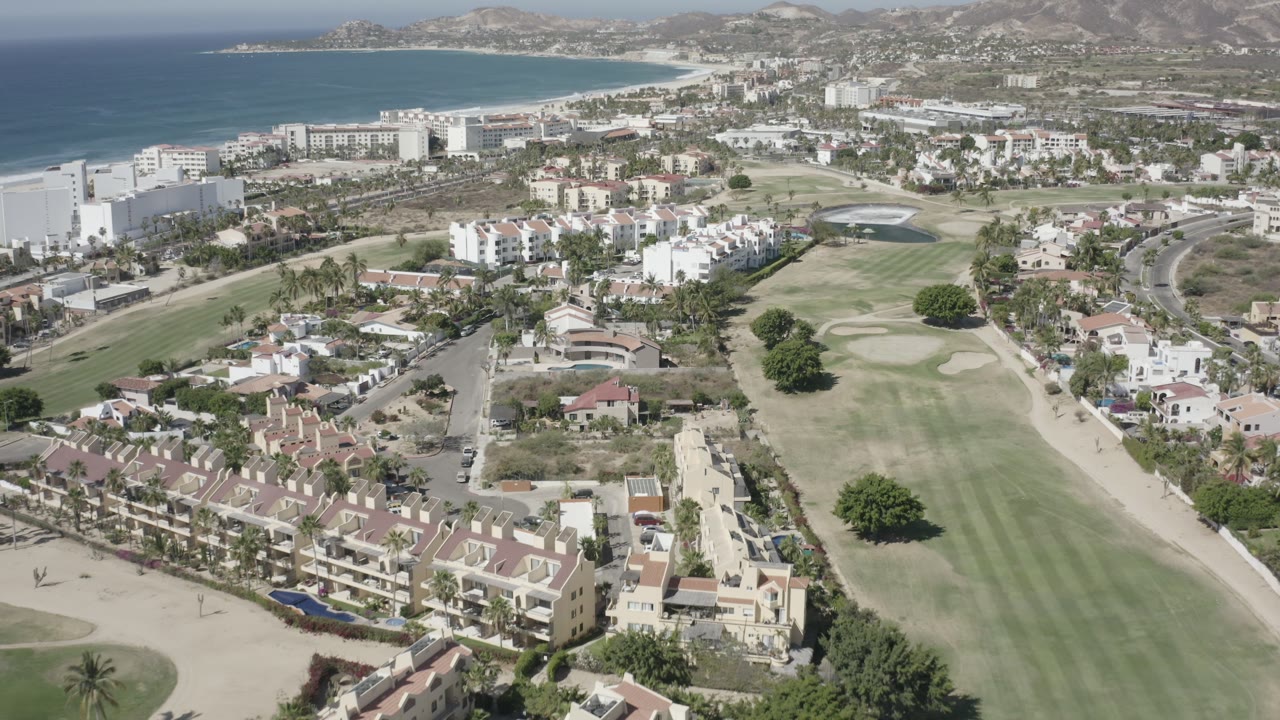 Aerial view over a golf course, homes, resort buildings, ocean, and hills.