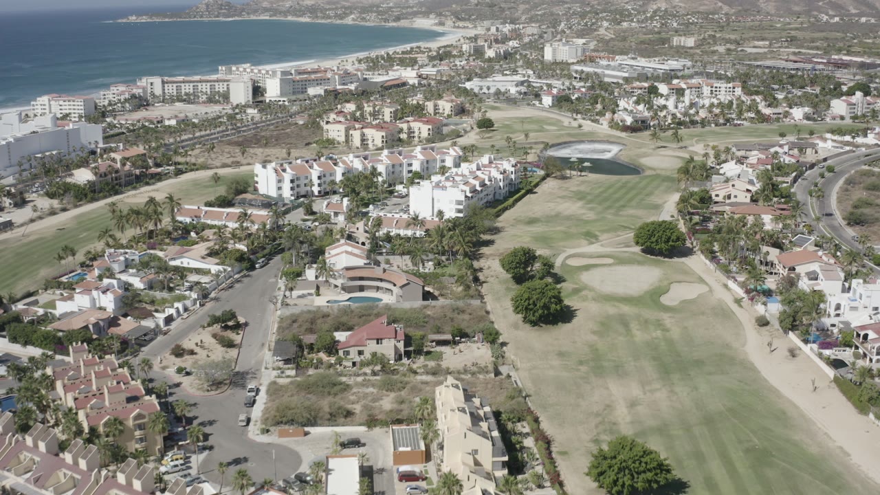 Aerial view over homes, golf fairways, beach buildings, and ocean.