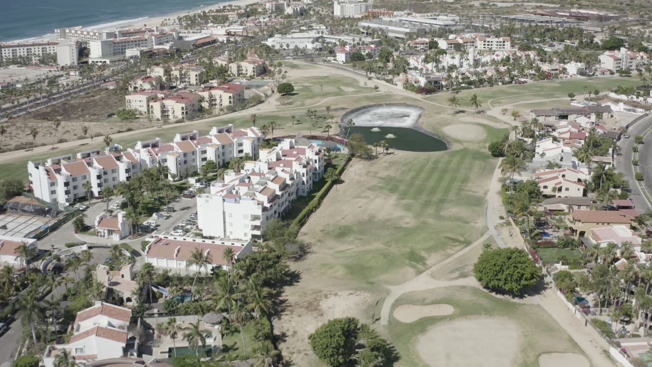 Aerial view of residential buildings beside a golf fairway and pond near the coast.