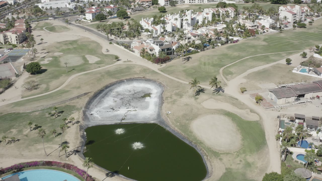 Aerial view of a golf course pond beside fairways and resort homes.