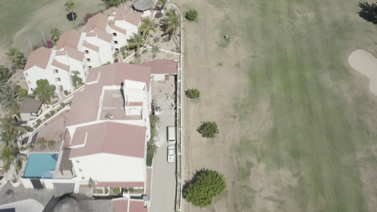 Aerial view of white buildings beside a golf fairway and pool.