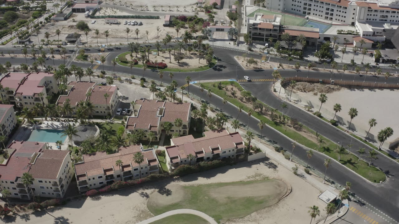 Top view of a road junction, sandy lots, palm trees, and large pale buildings.