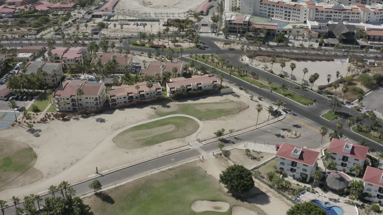 Aerial view of golf-course greens, sand traps, roads, and red-roof residential buildings.