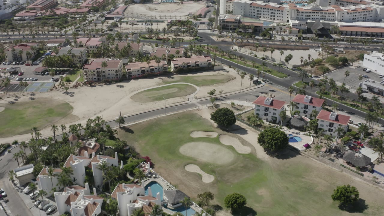 Oblique aerial of a golf green, sand traps, homes, and larger buildings.