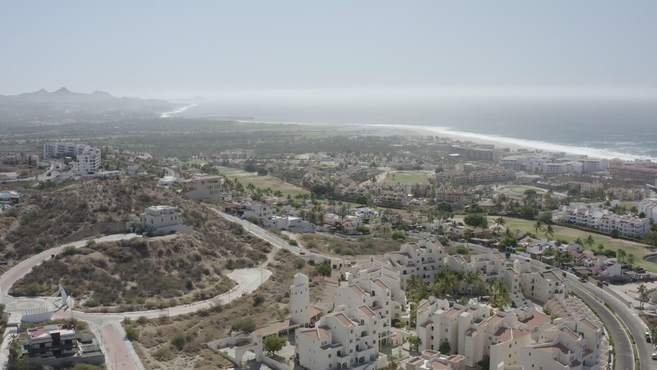Aerial view of hillside homes, roads, town blocks, beach, ocean, and hazy mountains.
