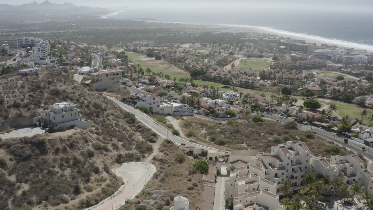Aerial view over dry hillside homes with ocean in the distance