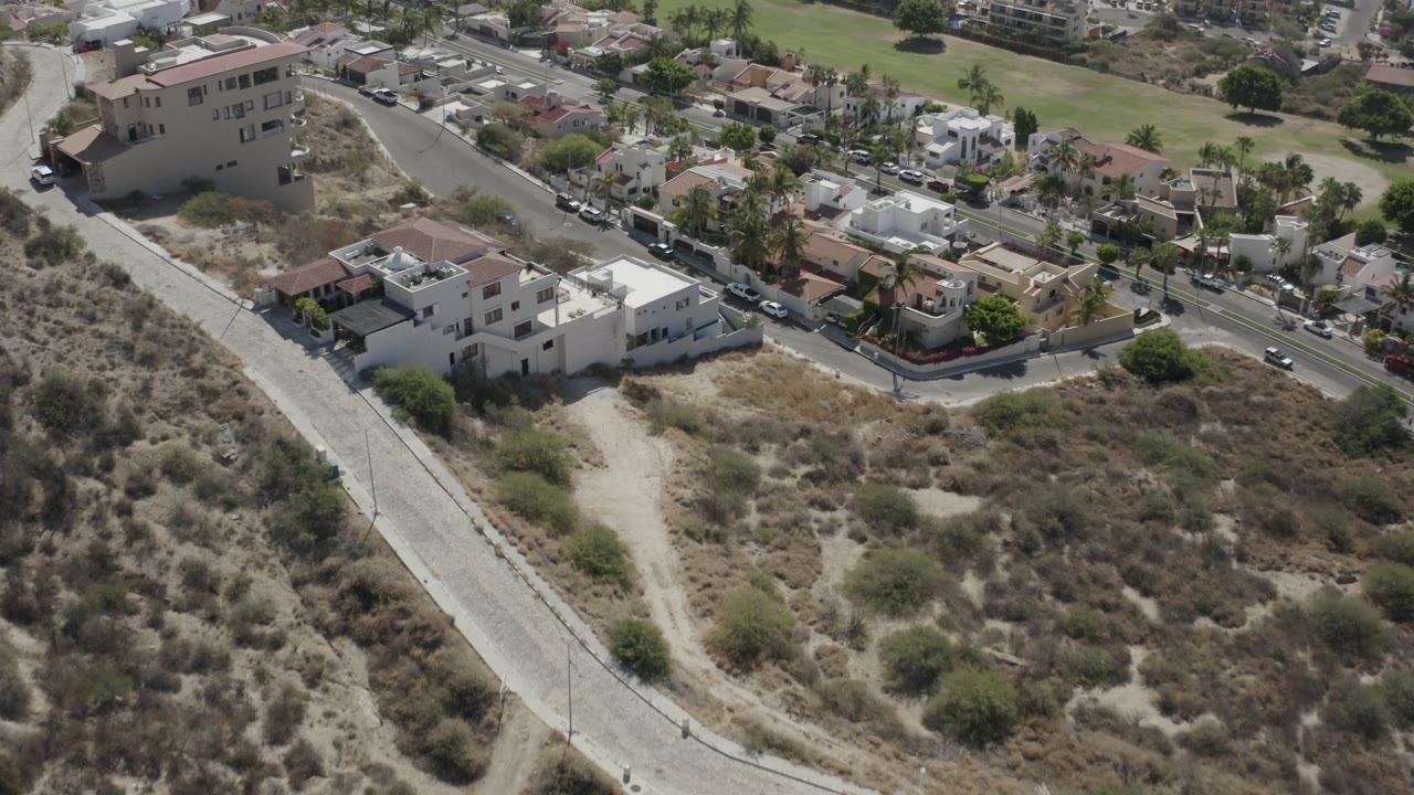 Aerial view of hillside homes beside a road and dry scrubland.