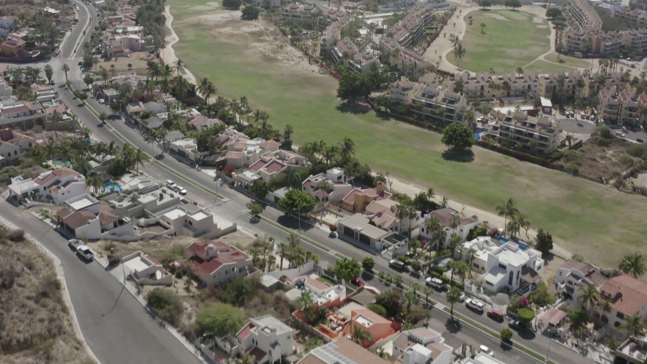 Aerial view of curved roads, homes, and green fairways near the coast.